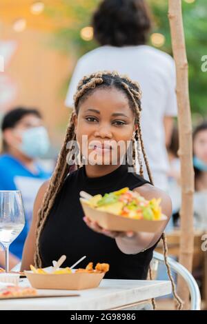 Latina Frau lächelt und bietet Fast Food an die Kamera Stockfoto