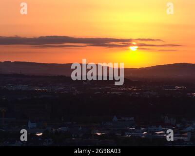 Atemberaubender Sonnenuntergang über der Stadt Koblenz mit Sonne, die durch Wolken am Horizont scheint, mit orangefarbenem, dramatischem Himmel und Licht, das von den Gebäudedächern reflektiert wird. Stockfoto