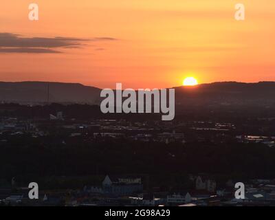 Majestätischer Sonnenuntergang über der Stadt Koblenz mit strahlender Sonne am Horizont und orangefarbenem, dramatischem Himmel mit Licht, das sich in den Gebäudedächern widerspiegelt. Stockfoto