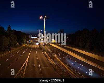 Blick auf die Bundesstraße B9, die durch das Zentrum von Koblenz führt, beleuchtet von Laternen mit gelbem Licht und nachts vorbeifahrenden Autos mit Bäumen. Stockfoto