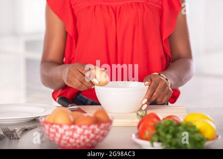 Nahaufnahme einer afroamerikanischen Frau, die ein Ei an den Rand einer Schüssel hält Stockfoto