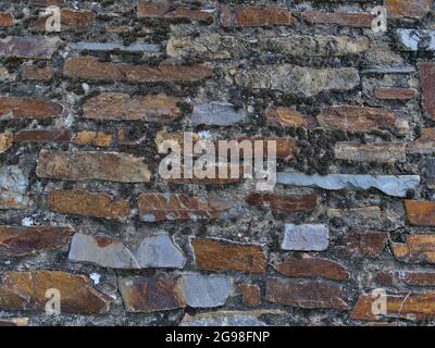 Nahaufnahme der alten Steinmauer mit orange und grau gemusterten Felsen und trockenen Flechten dazwischen. Stockfoto