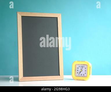 Leere Tafel mit gelbem Wecker auf blauem Hintergrund. Speicherplatz kopieren. Stockfoto