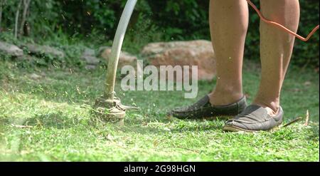 Mann mäht Rasen des Gartens mit elektrischen Rasentrimmer Maschine. Stockfoto