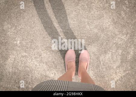 Draufsicht auf eine Frau, die in rosa Schuhen mit Schatten auf der Straße steht. Speicherplatz kopieren. Stockfoto