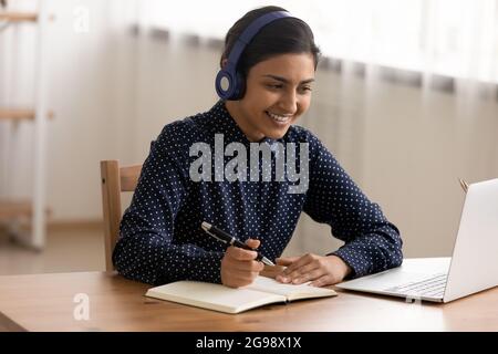 Nahaufnahme einer lächelnden Inderin mit Kopfhörern, die sich Notizen machen Stockfoto