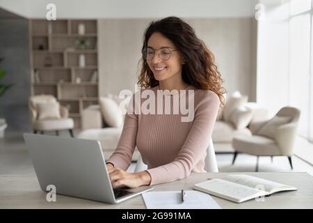 Lächelnde hispanische Frau arbeitet online auf dem Laptop zu Hause Stockfoto