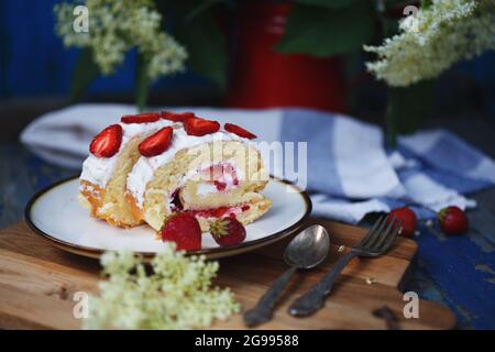 Biskuitrolle mit Erdbeeren. Ein Stück Dessert auf einem Teller. Rose und Erdbeere zur Dekoration Stockfoto