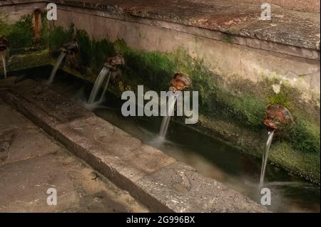 Das Wasser der Bergquelle strömt aus dem Löwenkopf in einen Kanal, bevor es zu rechteckigen Waschtischen mit Steinhängen zum Schrubben von Kleidungsstücken übergeht, die von hartnäckigen Verschmutzungen und Flecken befreit sind, im Lavatoio Medievale (mittelalterliches Waschhaus) in Cefalu, Sizilien, Italien. Jahrhundertelang reinigten die Wascherinnen von Cefalu hier im Wasser des Flusses Cefalino Kleidung und verwendeten Steinhänge, um Kleidungsstücke von hartnäckigem Schmutz und Flecken zu schrubben. Der sizilianische Dichter Vincenzo Auria beschrieb Cefalinos Wasser als „reiner als Silber, kälter als Schnee“. Stockfoto