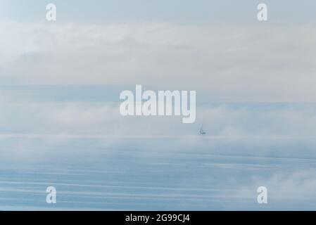 Segelboot, das auf hoher See mit Wolken und Nebel segelt. Stockfoto