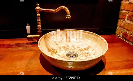 Vintage schöner Wasserhahn und goldene Mischbatterie auf einem runden Marmorwaschbecken im Badezimmer. Innen eine teure Toilette mit einem Marmorwaschbecken. Stockfoto