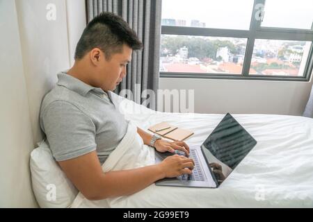 Junger Mann, der im Schlafzimmer arbeitet Stockfoto