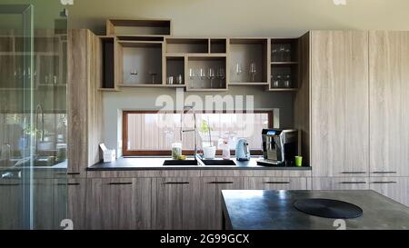 Ukraine, Kiew - 24. September 2019: Moderne Küche mit braunen Holzmöbeln, Steinplatten, Waschbecken und Wasserhahn. Eine Kaffeemaschine steht auf dem Tisch. Stockfoto