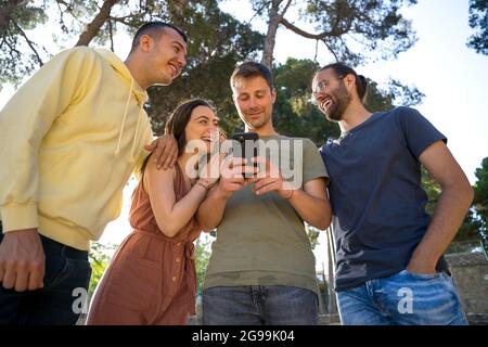 Freunde, die mit ihren Handys lachen. Sie schauen sich gegenseitig an. Sie sind jung und kaukasisch. Nahaufnahme.Sie tragen farbenfrohe Sommerklumpen Stockfoto