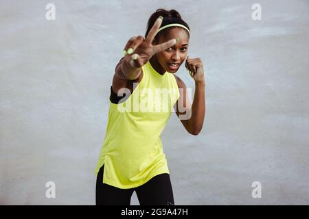 Afrikanische Frau in Fitness tragen zeigen Friedenszeichen mit ihrer Hand während des Trainings. Junge Frau beim Training vor weißem Hintergrund. Stockfoto