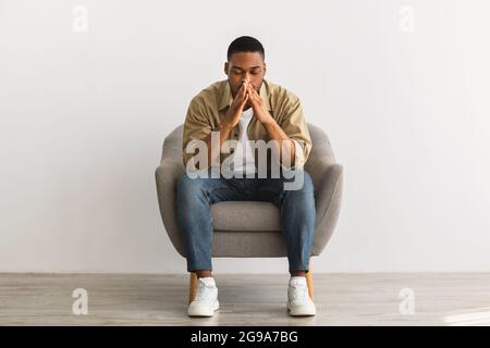 Frustrierter Afrikanischer Kerl, Der Über Probleme Denkt, Die Über Der Grauen Wand Sitzen Stockfoto
