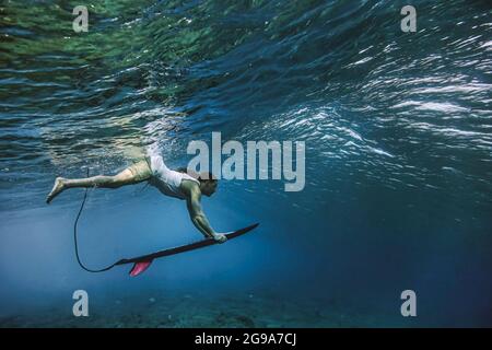 Männlicher Surfer mit Surfbrett während des Tauchens unter Wasser auf den Malediven Stockfoto