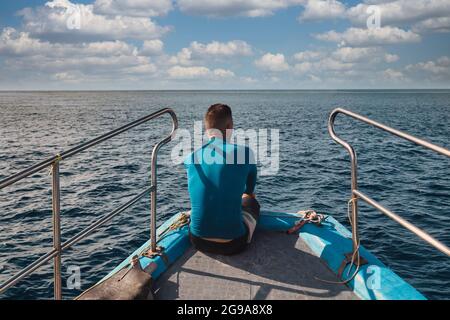 Rückansicht eines Mannes, der auf einem Bug eines Bootes sitzt und auf das Meer blickt Stockfoto