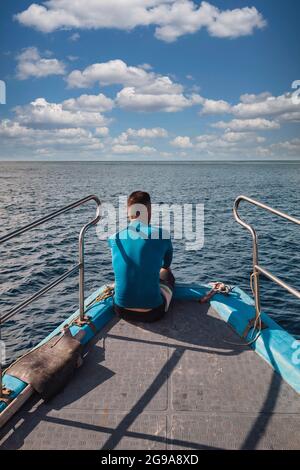 Rückansicht eines Mannes, der auf einem Bug eines Bootes sitzt und auf das Meer blickt Stockfoto