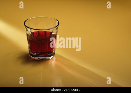 Heller Lichtstrahl über einem Glas Red Juice Drink auf einem gelben Sandhintergrund mit Kopierfläche. Stockfoto