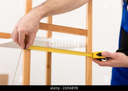 Beschnittene Aufnahme Von Zimmerer, Die Holzregal Mit Klebeband Im Innen-Bereich Messen Stockfoto