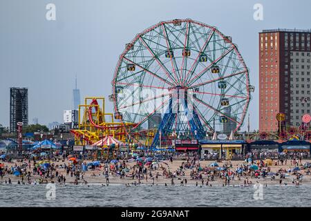 Die Menschen genießen den Strand vor dem One World Trade Center in Lower Manhattan und das Wonder Wheel auf Coney Island in New York. Stockfoto