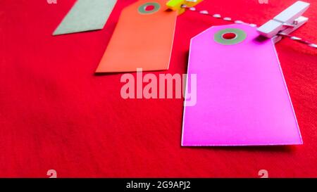 Bunte Papiernotizen und Wäscheklammern auf rotem Hintergrund. Leere Farbe Karton Preisschilder, Verkauf Anhänger, Geschenk-Tag, Adresse Etikett, Gepäckanhänger hängen o Stockfoto