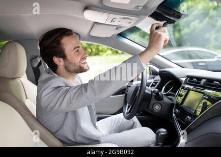 Mann, der im Auto sitzt und den Rückspiegel justiert, den Innenraum des Autos, den Weg zum Büro Stockfoto