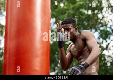 Muskulöser schwarzer Profi-Boxer schwitzt in Handschuhen beim Boxtraining im Freien, junger afroamerikanischer Boxer beim Training auf dem Straßenspielplatz. Stockfoto