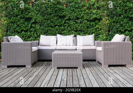 Schöne Holzterrasse mit Rattan-Gartenmöbeln mit grünem Hintergrund. Stockfoto