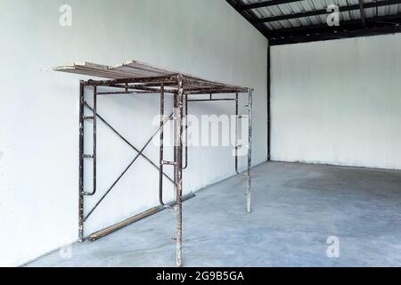 Installation von Gerüsten für den Innenbau und die Lackierung der Betonwand des Lagerhauses. Leerer weißer Raum mit Gerüsten. Altes Haus während der Renovierung. Stockfoto