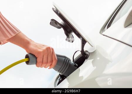 Frau, die einen Ladestecker oder ein Ladegerät in ein weißes Elektroauto steckt Stockfoto