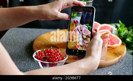 Eine Frau fotografiert am Telefon Grapefruitlimonade. Flach legen ein erfrischendes kaltes Getränk im Sommer Stockfoto