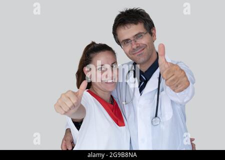 Arzt und Krankenschwester umarmen sich lächelnd und zeigen Daumen nach oben. Konzept der Zusammenarbeit zwischen Arzt und Krankenschwester Stockfoto