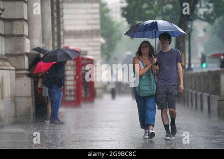 Ein junges Paar läuft entlang der Parliament Street in Westminster, während starker Regen durch das Zentrum Londons fegt. Gewitter, die Blitze und sintflutartige Regenfälle in den Süden bringen, werden bis Montag anhalten, sagten Prognostiker. Bilddatum: Sonntag, 25. Juli 2021. Stockfoto