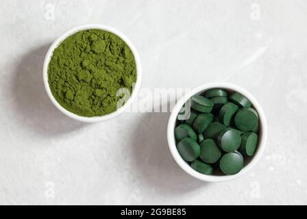 Chlorella und Spirulina aus der Nähe. Spirulina Pillen und Chlorella Pulver in Schalen auf weißem Beton Hintergrund. Superfoods. Draufsicht, flach liegend. Stockfoto