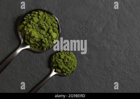 Chlorella oder Spirulina Pulver in Löffeln auf dunklem Grund. Grünalgenpulver. Organische Mineralergänzung. Entgiftung. Platz zum Kopieren, Draufsicht, flach liegend. Stockfoto