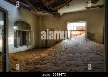 Verlassene Gebäude, die in der alten Diamantabbaustadt Kolmanskop in der Nähe von Luderitz, Namib-Wüste, Namibia, von eindringenden Sand übernommen wurden. Stockfoto