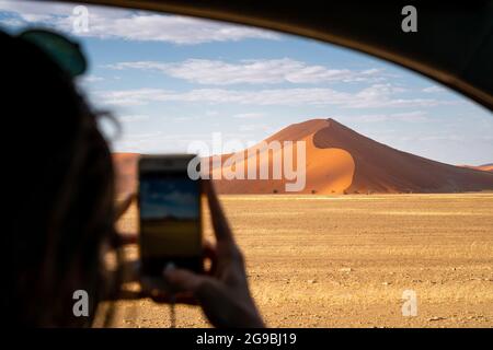 Tourist, der ein Handy-Foto von einer riesigen Sanddüne in der Nähe von Sossusvlei im Namib-Naukluft Nationalpark macht, Namibia, Afrika. Stockfoto