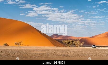 Touristenfahrzeug neben einer hoch aufragenden Sanddüne in der Nähe von Sossusvlei im Namib-Naukluft National Park, Namibia, Afrika. Stockfoto