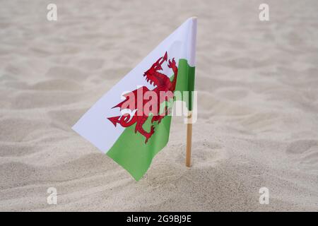 Walisische Flagge winkt im Wind am Sommerstrand. Flagge von Wales auf Sandgrund Stockfoto
