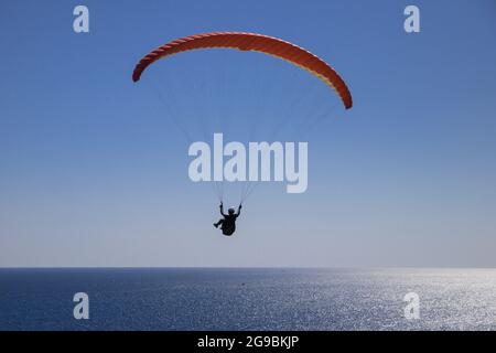 Ein mutiger Mann fliegt an einem sonnigen Tag mit einem Gleitschirm über das offene Meer. Touristenattraktion im Badeort. Stockfoto