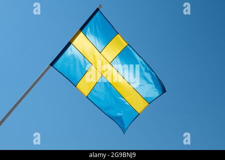 Flagge Schwedens auf blauem Himmel Hintergrund. Schwedische Flagge winkt bei Wind und Sonnenlicht Stockfoto