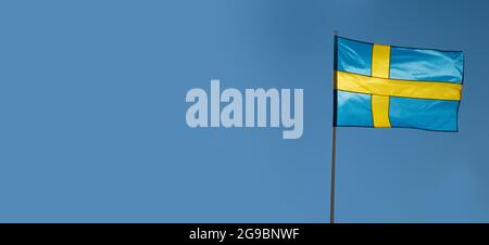 Flagge Schwedens auf blauem Himmel Hintergrund. Leerer Kopierbereich für Text. Schwedische Flagge winkt bei Wind und Sonnenlicht Stockfoto