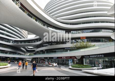 Peking, China. Juli 2021. Menschen, die Gesichtsmasken tragen, gehen in die Nähe des Einkaufszentrums „Galaxy SOHO“ in Peking. Galaxy SOHO liegt in der East 2nd Ring Road, in der Nähe von Chaoyangmen, Peking. Es wurde 2012 fertiggestellt und von Zaha Hadid Architects, Großbritannien, auf einer Fläche von 334000 Quadratmetern (3595000 Quadratfuß) gebaut. (Foto von Sheldon Cooper/SOPA Images/Sipa USA) Quelle: SIPA USA/Alamy Live News Stockfoto