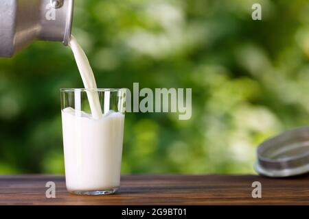 Milch, die aus Metallkännen in Glas gießt Stockfoto