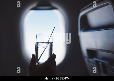 Passagier genießt ein Getränk während des Fluges. Mann, der ein Glas Gin Tonic gegen das Flugzeugfenster hält. Stockfoto