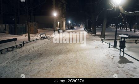 Krakau, Polen 03.02.2021 Schneebedeckte Straße in der Altstadt Hauptmarkt. Krakau, Polen. Straßenlaternen sind beleuchtet. Menschen, die während der Wintersaison auf der verschneiten Straße spazieren. Hochwertige Nigcaht-Zeitaufnahme. Stockfoto