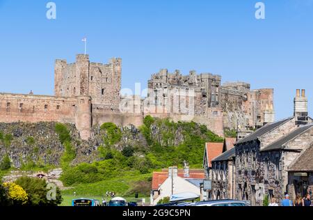 Das ikonische Bamburgh Castle, ein denkmalgeschütztes Gebäude an der Nordostküste Englands, das vom Dorf Bamburgh in Northumberland auf einem sonnigen Tal aus gesehen wird Stockfoto