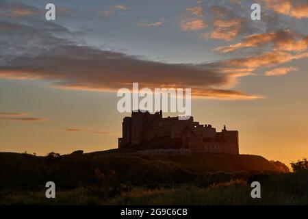 Das berühmte Schloss Bamburgh an der Nordostküste Englands, neben dem Dorf Bamburgh in Northumberland, das bei Sonnenuntergang zur goldenen Stunde auf der Skyline zu sehen ist Stockfoto